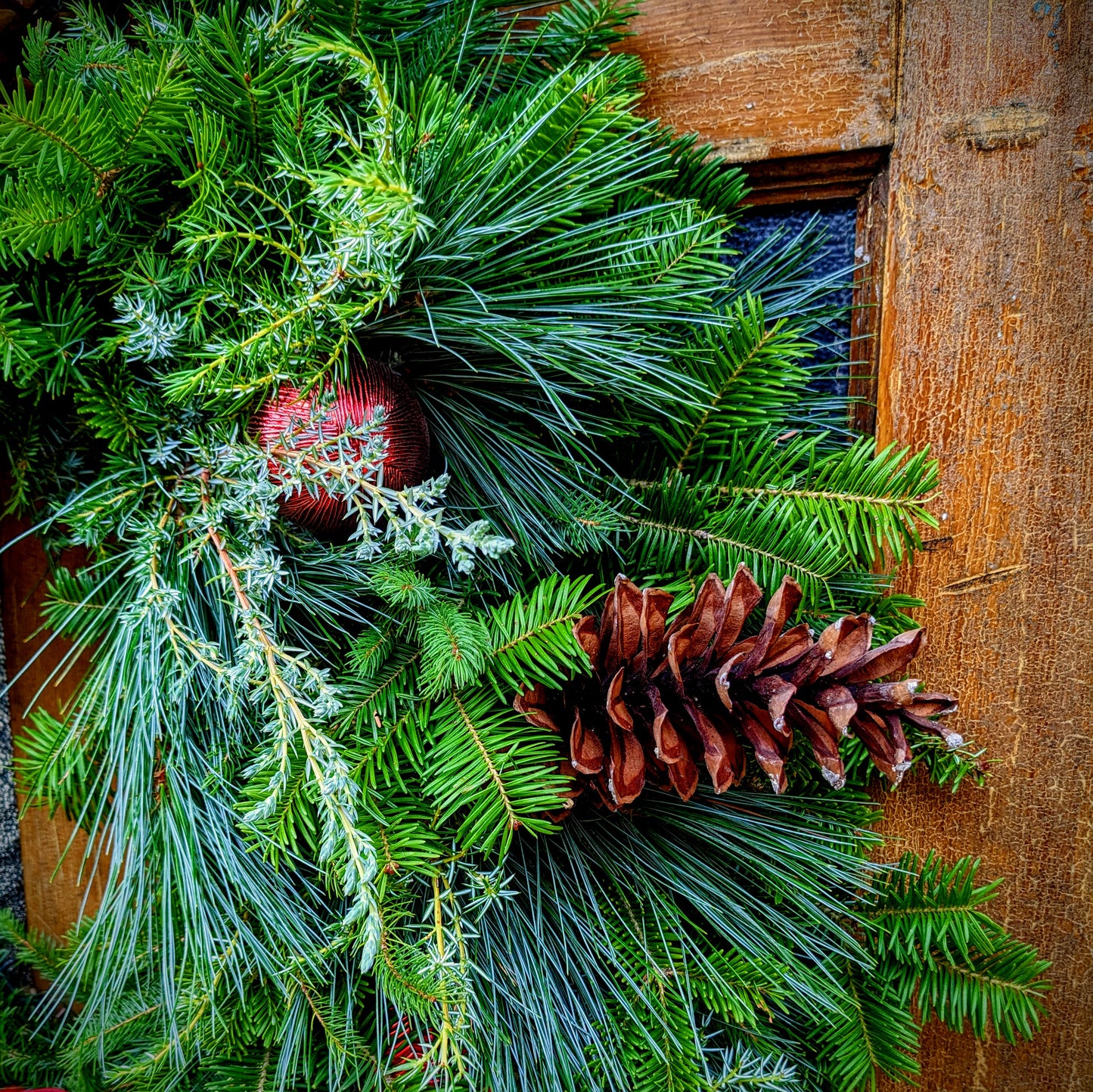 Christmas wreath with pine cones and red ball on a wooden background